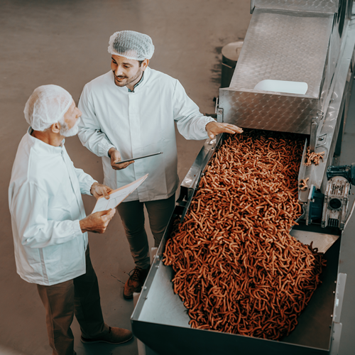 Empleados de una industria de alimentación al lado de una cinta transportadora de alimentos
