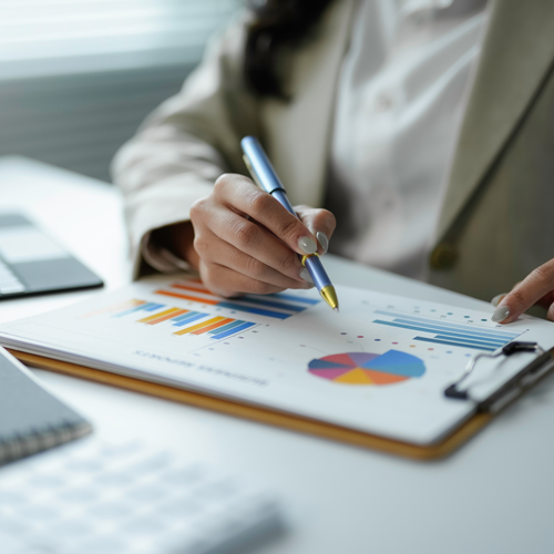 Persona de negocios examinando informes financieros, trabajando con tablas y gráficos en una mesa de oficina.